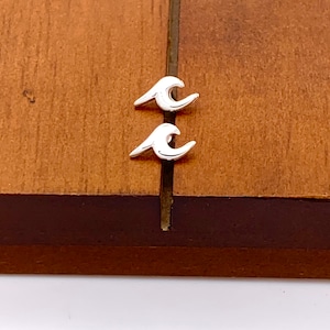 May include: A pair of silver wave earrings on a wooden surface.