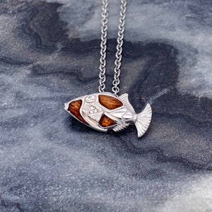 May include: A silver chain necklace with a wooden and silver fish pendant. The fish has a detailed design and is accented with small diamonds.