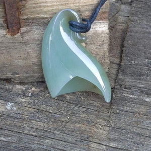 May include: A green jade pendant shaped like a wave, hanging from a black cord.