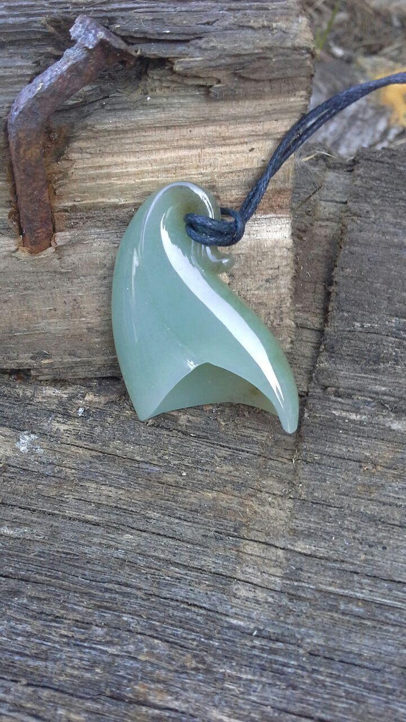 May include: A green jade pendant shaped like a wave, hanging from a black cord.