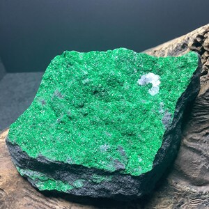 Könnte beinhalten: Ein großer, rauer, grüner Stein mit einer dunkelgrauen Basis. Der Stein ist mit kleinen, glitzernden grünen Kristallen bedeckt.