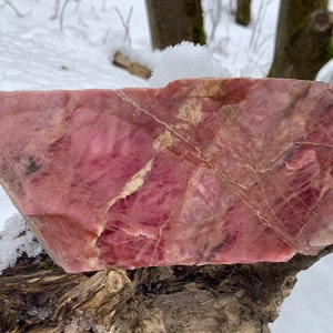 May include: A large, irregularly shaped piece of pink and white rhodochrosite, a type of mineral, with a smooth, polished surface. The stone has a variety of pink and white hues and is veined with white.