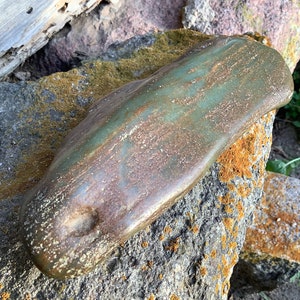May include: A large, smooth, green and brown rock with a rounded shape. The rock has a mottled appearance with streaks of green, brown, and white.