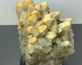 Op de afbeelding: Een cluster van natuurlijke mineraalkristallen met doorschijnende, heldere basisformaties bekroond met opvallende, ondoorzichtige gele, piramidevormige punten. Het exemplaar vertoont een ruw, getextureerd oppervlak met gevarieerde geometrische kristalstructuren.
