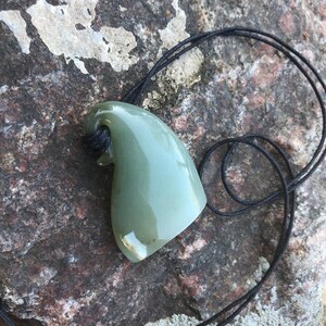May include: A green jade pendant shaped like a shark fin, hanging from a black cord.