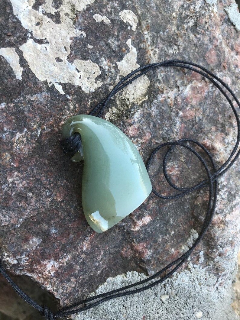 May include: A green jade pendant shaped like a shark fin, hanging from a black cord.