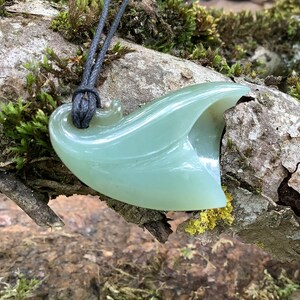 May include: A pale green jade pendant shaped like a leaf, hanging from a black cord. The pendant is carved with intricate details and has a smooth, polished finish.