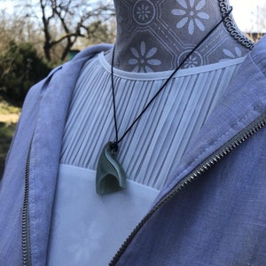 May include: A light blue jacket with a zipper and a white shirt with a green jade pendant necklace.