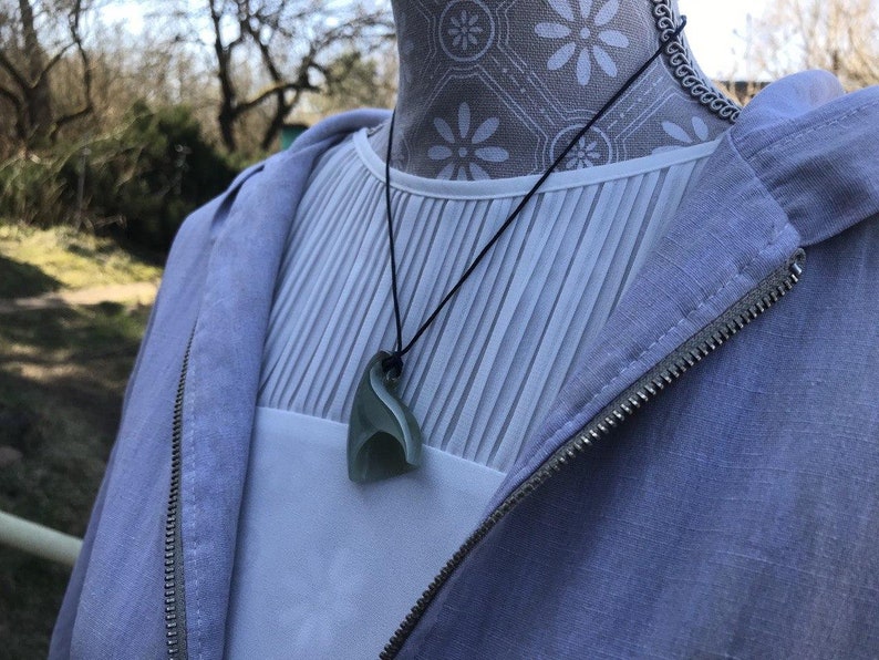 May include: A light blue jacket with a zipper and a white shirt with a green jade pendant necklace.