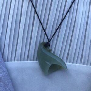 May include: A green jade pendant shaped like a bird, hanging from a black cord necklace.