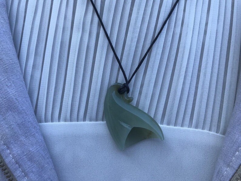 May include: A green jade pendant shaped like a bird, hanging from a black cord necklace.