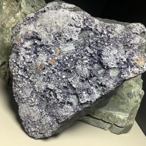May include: A large, rough, gray rock with purple and white crystals embedded in it. The rock has a rough, uneven surface.