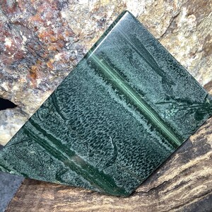 May include: A green and white patterned stone slab with a smooth, polished surface. The stone has a unique, natural pattern with streaks and swirls of color.