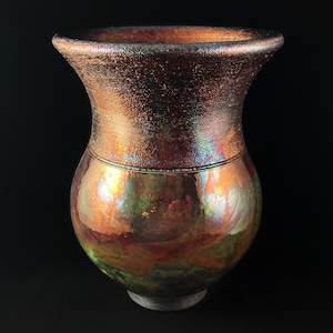 May include: A handcrafted ceramic vase with a unique iridescent glaze. The vase features a bulbous body and a flared rim. The glaze transitions from copper to green and purple hues, creating a striking visual effect. The vase is approximately 8 inches tall.