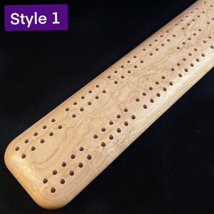 May include: A light wood cribbage board with a natural wood grain finish and a pattern of holes drilled into the surface. The board is labeled "Style 1".