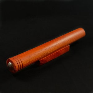 May include: A wooden kaleidoscope with a red finish and a small, round viewing window. The kaleidoscope is resting on a wooden stand.