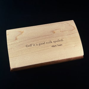 Op de afbeelding: Een houten doos met een citaat van Mark Twain: "Golf is een goede wandeling die verpest is."