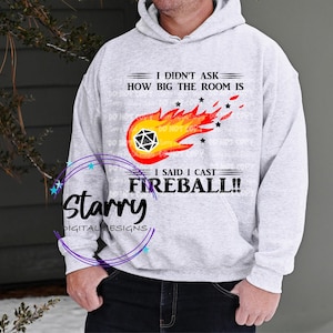 May include: A light gray hoodie with the text "I DIDN'T ASK HOW BIG THE ROOM IS, I SAID I CAST FIREBALL!!" and a graphic of a fireball with a D20 die. The hoodie also has the text "Starry DIGITAL DESIGNS".