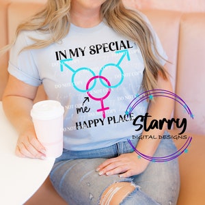 May include: A light blue t-shirt with the text "IN MY SPECIAL HAPPY PLACE" and gender symbols in blue and pink. The shirt is worn by a person holding a pink and white paper cup.