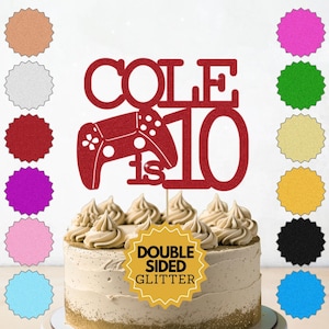 May include: A red glitter cake topper with the name "COLE", a controller graphic, and the number "10". The topper is on a frosted cake. Various colour samples are shown in the background.