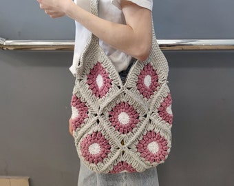 May include: A crocheted tote bag with a pink and white floral pattern. The bag is made of a soft, lightweight yarn and has a spacious interior.