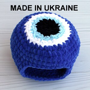May include: Blue crocheted evil eye charm with a white, light blue and black eye design. "MADE IN UKRAINE" is written in black text at the top of the image.