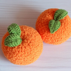 Op de afbeelding: Twee gehaakte oranje pluche speelgoedjes met groene bladeren. De speelgoedjes zijn oranjevormig en hebben een pluche textuur.