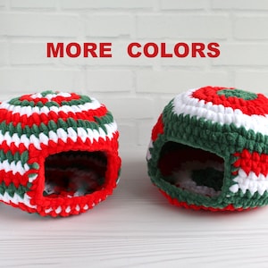 Può includere: Due lettini per animali domestici all'uncinetto in rosso, verde e bianco. I lettini sono a forma di cupola con un'apertura nella parte anteriore. Il testo "MORE COLORS" è visualizzato sopra i lettini. I lettini sono progettati per piccoli animali domestici.