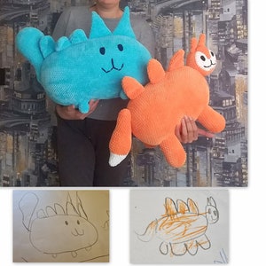 May include: Two crocheted stuffed toys, one blue and one orange, are being held by a person. The blue toy is a cat with a dinosaur-like back. The orange toy is a cat with a dinosaur-like tail.  Next to the toys are two drawings of the toys, one in black and white and one in orange and brown.
