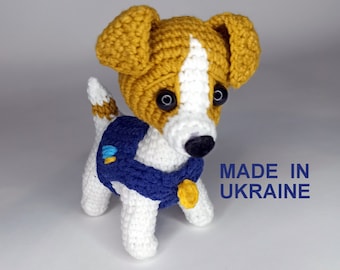 May include: Crocheted Jack Russell terrier dog toy with white and brown fur, wearing a blue vest with a yellow tag. The toy is made in Ukraine.