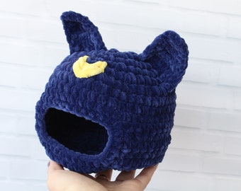 Puede incluir: Un gorro azul de crochet con un diseño de media luna amarilla y dos orejas caídas.