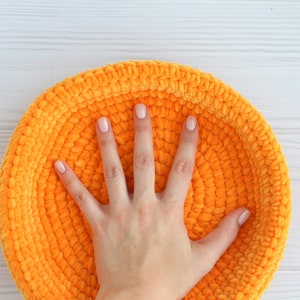 May include: A bright orange crocheted bowl with a soft, fuzzy texture. The bowl is large enough to fit a hand inside.