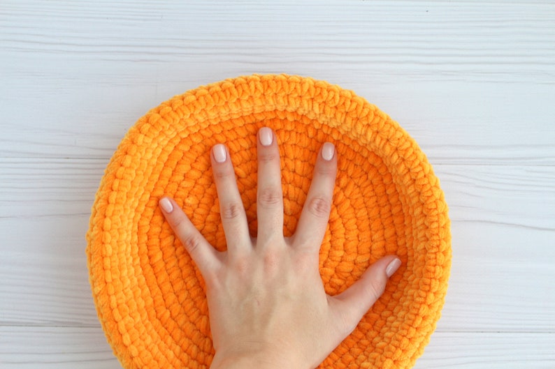 May include: A bright orange crocheted bowl with a soft, fuzzy texture. The bowl is large enough to fit a hand inside.