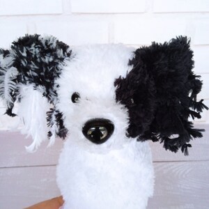 Puede incluir: Un perro de peluche blanco y negro con pelo esponjoso. El perro tiene ojos negros y una nariz negra.