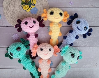 May include: Six crocheted axolotl plushies in different colors, including pink, yellow, blue, green, and orange. The plushies have large eyes and a smiling expression.