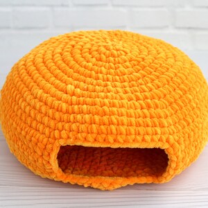 May include: A bright orange crocheted pet bed shaped like a dome with a round opening. The bed is made of soft, fuzzy yarn and is perfect for small pets.