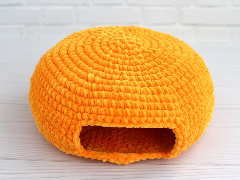 May include: A bright orange crocheted pet bed shaped like a dome with a round opening. The bed is made of soft, fuzzy yarn and is perfect for small pets.