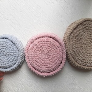 May include: Three round crocheted baskets in different sizes. The largest basket is brown, the middle basket is pink, and the smallest basket is light blue.