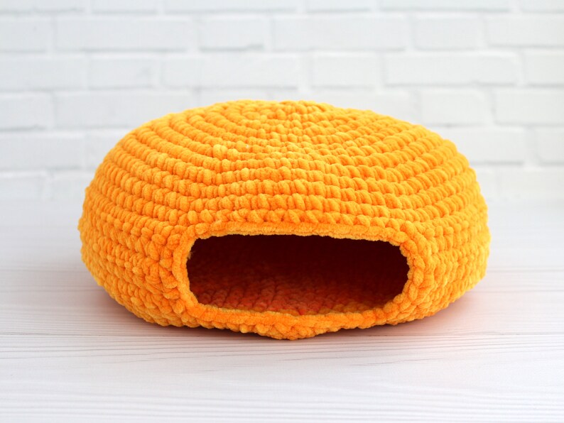 May include: A bright orange crocheted cat bed shaped like a dome with a round entrance hole.