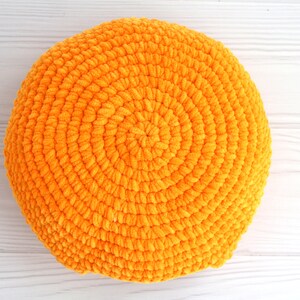 May include: A round, orange crocheted pillow with a textured surface.