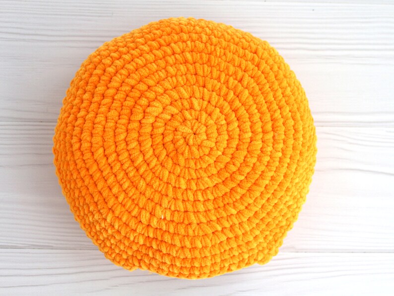 May include: A round, orange crocheted pillow with a textured surface.