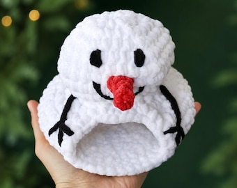 May include: A white crocheted snowman hat made of soft, plush yarn. The hat features a round top, a bright red carrot-shaped nose, black embroidered eyes, a black curved mouth, and black stick-like arms stitched onto the sides of the base.