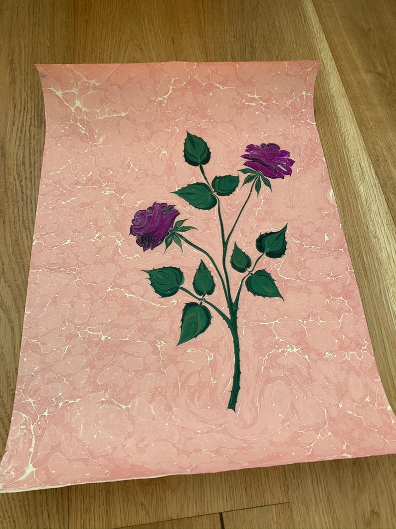 May include: A pink marbled paper with a hand-painted design of two purple roses with green leaves and stems.