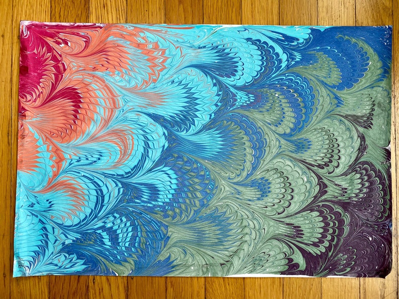 May include: Abstract marbled paper with a gradient of colors, starting with red and orange at the top, transitioning to blue and green, and ending with dark purple and black at the bottom. The marbling creates a swirling, feather-like pattern.