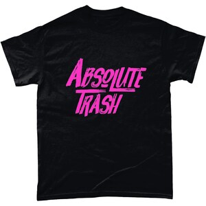 以下が含まれることがあります： ピンクのグラフィックが施された黒いTシャツ。スタイリッシュなフォントで「ABSOLUTE TRASH」と書かれています。