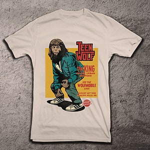 May include: A white t-shirt with a vintage-style graphic of a werewolf. The graphic features the text "Teen Wolf", "The King of the Urban Sniffers!" and "See the Wolfmobile Live!" with a date and location.