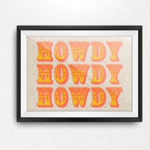 Peut inclure: Une impression encadrée avec le mot "HOWDY" répété trois fois dans une police rétro. Les lettres sont orange et jaunes avec un fond texturé.