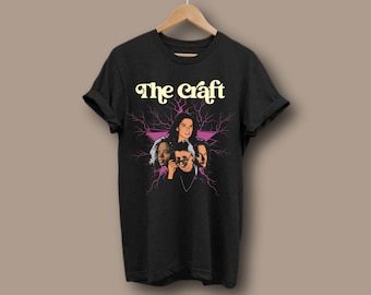 Könnte beinhalten: Schwarzes T-Shirt mit einem Grafikdruck der vier Hauptfiguren aus dem Film "The Craft" in einem rosa Stern mit Blitzen. Der Text "The Craft" ist in Gelb.