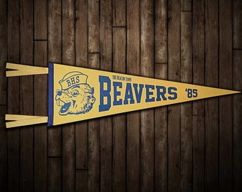 May include: A yellow pennant with blue trim and text. The pennant features a cartoon beaver wearing a sailor hat and the text "BHS The Beacon Town BEAVERS '85".