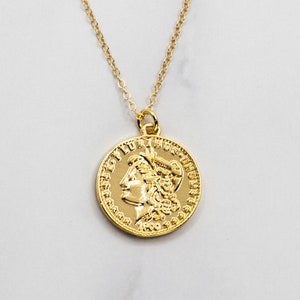May include: A gold chain necklace with a gold coin pendant featuring a profile of a woman with a crown.
